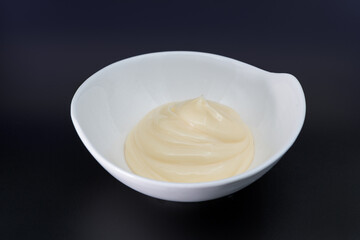white souce in white dish on black, dark background