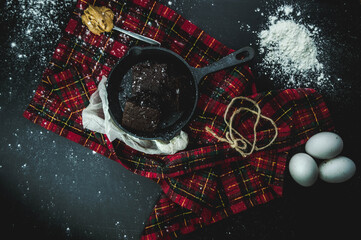 Brownies de chocolate cortados en cuadrados, con una cucharada de mantequilla de mani. Sarten de Hierro partido. Sobre un fondo de cuadrito en un fondo negro. Concepto de fotograf&iacute;a de comida oscura.