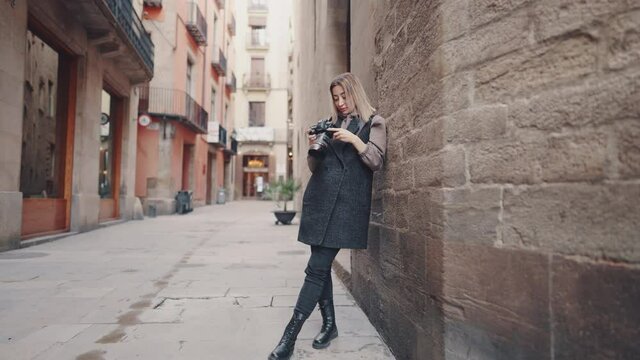 Beautiful Female tourist with dslr photo camera walking through old town narrow streets, Barcelona, Spain. She takes photos and chooses best