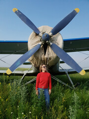 Woman portrait in front of an old aircraft. Young beautiful woman with red jacket stand in front of older bomber aircraft with a propeller in background. Photo shoot near the plane.
