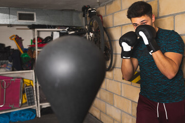 Young caucasian man boxing with a boxing bag at the garage	
