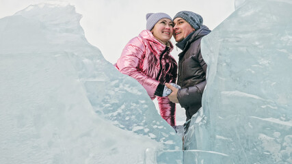 Couple has fun winter walk against background of ice of frozen lake. Lovers lie on clear ice with...