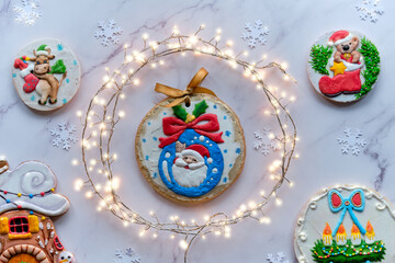 Fototapeta na wymiar Decorated gingerbread with various motives, assortment of tasty traditional children gifts for Xmas. Christmas flat lay with festive garland in circle. Top view on white marble background.