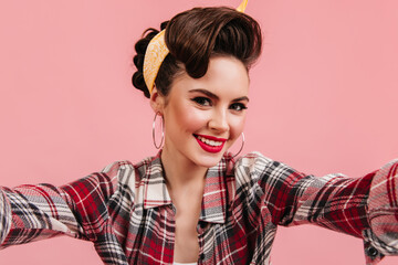 Lovely young woman in checkered shirt smiling on pink background. Emotional pinup girl taking...