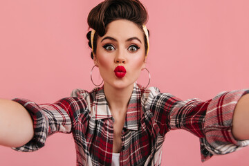Jocund pinup girl posing in red checkered shirt. Amazed woman taking selfie with kissing face...