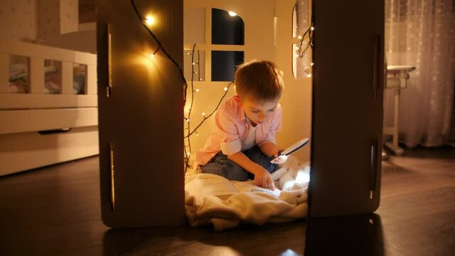 Cute boy reading book at night with flashlight. Concept of child education and reading in dark room