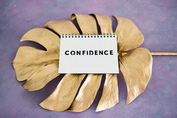 Confidence notepad on top of golden leaf on pink background, psychology and attitude