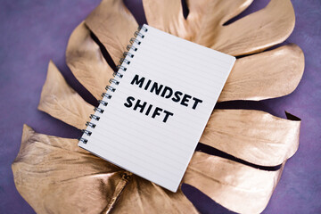 Mindset Shift notepad on top of golden leaf on pink background, psychology and attitude