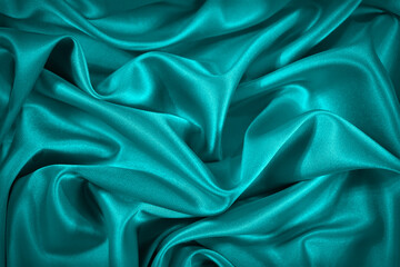 Blue and green silk satin fabric. Elegant teal color background. Liquid wave or silk soft wavy folds. Beautiful turquoise fabric background with copy space for your design.