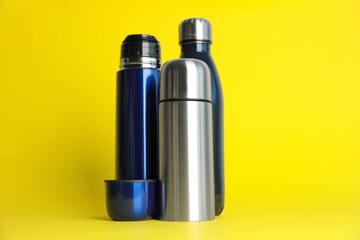 Stylish stainless thermo bottles on yellow background