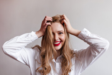 Magnificent young girl touching blonde hair with smile. Studio shot of stylish female model in shirt.
