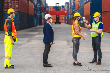 Professional of group cargo foreman in helmets standing and using infrared thermometer for checking body temperature staff fever before work in quarantine for coronavirus wearing protective mask