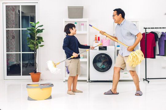 Father Teaching Asian Kid Little Boy Son Having Fun Doing Household Chores Cleaning And Washing Floor Wiping Dust With Mopping And Vacuum Cleaner While Cleaning House Together At Home