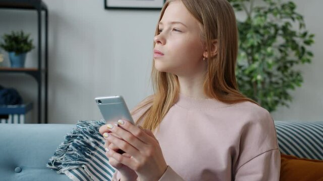 Slow motion of serious teen child using smartphone messaging indoors in apartment. Online communication and modern technology for children concept.