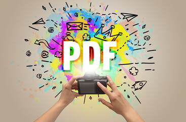 Close-up of a hand holding digital camera with abstract drawing and PDF inscription