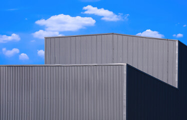Fototapeta na wymiar Low angle view of gray corrugated metal factory building against white clouds in blue sky background