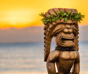 Hawaiian Tiki Statue with an amazing sunrise in the background. The tiki is dressed up with traditional leaves and a macadamia necklace. It is made of wood and looks large in size. - obrazy, fototapety, plakaty