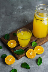Obraz na płótnie Canvas Es jeruk peras or orange juice iced with cut of sweet oranges. Served on clear glass on wooden rustic board. Grey grainy background. 