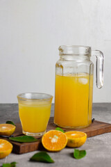 Es jeruk peras or orange juice iced with cut of sweet oranges. Served on clear glass on wooden rustic board. Grey grainy background. 