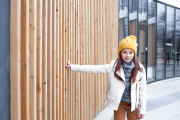 Preteen girl dressed yellow hat, jacket and trousers walking outdoor in the street of the city