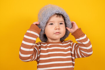 Handsome baby boy puts gray knitted hat on yellow background. Hipster style. Head in warm hat. Fashion concept. Winter clothes and accessories.