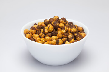 Crunchy Roasted Chana Masala in a white bowl, made with Bengal Grams or Chickpeas. Pile of Indian spicy snacks (Namkeen), under top lighting, side view, against the white background.