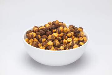 Crunchy Roasted Chana Masala in a white bowl, made with Bengal Grams or Chickpeas. Pile of Indian spicy snacks (Namkeen), under top lighting, side view, against the white background.