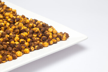 Crunchy Roasted Chana Masala in a white ceramic square plate, made with Bengal Grams or Chickpeas. Pile of Indian spicy snacks (Namkeen), under top lighting, side view, against the white background.