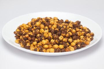 Crunchy Roasted Chana Masala in a White Ceramic plate, made with Bengal Grams or Chickpeas. Pile of Indian spicy snacks (Namkeen), under top lighting, side view, against the white background.