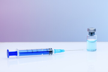 The Coronavirus Vaccine and syringe injection. Vial with vaccine against coronavirus on a light blue and pink gradient background. The concept of protection against coronavirus infection, COVID-19