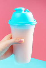 Hand holds a shaker with protein shake on pink and blue background.