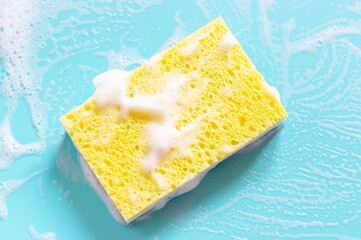 Yellow sponge with foam on a blue background close-up.