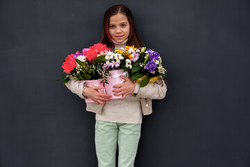 Little kid holding the bouquet of flowers and posing against the wall at the street.