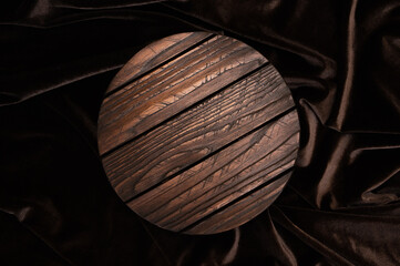 Dark brown round wooden podium for product display on wavy satin background. Empty textured wooden...