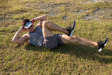 An asian athlete performs bicycles crunches on the ground at a city park outdoors. Cardio workout,...