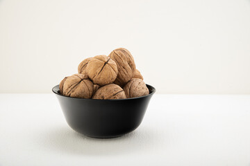 Unpeeled walnuts in a shell in a black glass bowl on a light background