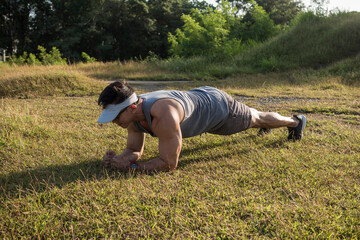 An athletic asian man does planks on the grass at a open field outdoors. Core and abdominal...