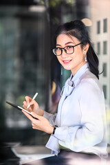 Portrait of young female entrepreneur holding digital tablet and smiling to camera while sitting in modern office.