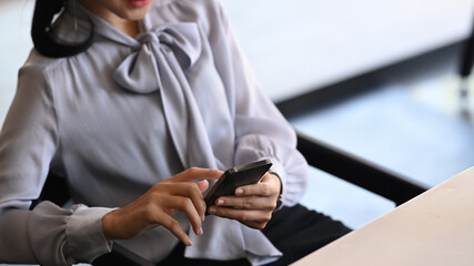 Cropped shot of young woman taking a break at her workspace checking her smart phone.