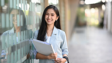 Fototapeta na wymiar Happy young asian businesswoman holding file and standing outside of office.