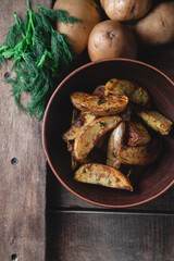 Delicious baked country potatoes in a earthen bowl with spices, dill and green onions, on a wooden table