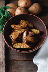Delicious baked country potatoes in a earthen bowl with spices, dill and green onions, on a wooden table