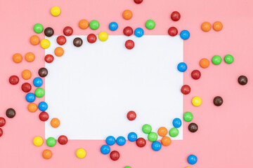 empty copy space for text white paper in the middle, top view of Colorful chocolate coated candy on pink background with valentines. Valentines day concept festive food gifts