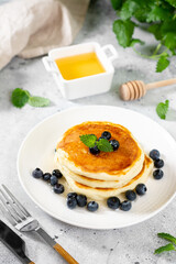 Pancakes in a white plate on the light gray kitchen table. Homemade delicious pancakes with honey and blueberries. Delicious sweet and hearty breakfast