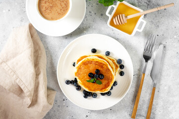 Pancakes in a white plate on the light gray kitchen table. Homemade delicious pancakes with honey...