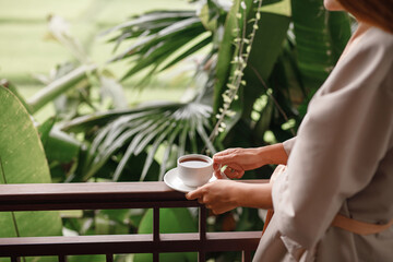 Woman holding cup of hot steaming drink tea on the  balcony with tropical view
