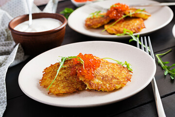 Fried potato pancakes with red caviar and sour cream, fritter, roesti. Traditional delicious food, lunch.