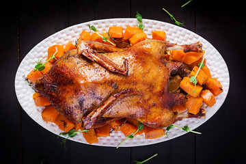 Homemade baked duck. Crispy whole roast duck. Thanksgiving or Christmas dinner. Roast duck with thyme and pumpkin on rustic wooden table. Top view, overhead