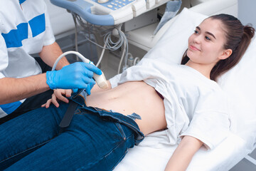 The young doctor makes an ultrasound of the abdominal cavity to a young beautiful girl. Ultrasound pregnancy
