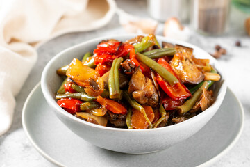 Pickled vegetables in a gray bowl on the light gray kitchen table. Different vegetables - red pepper, eggplant, carrots and peas in a bowl. Vegetarian dish